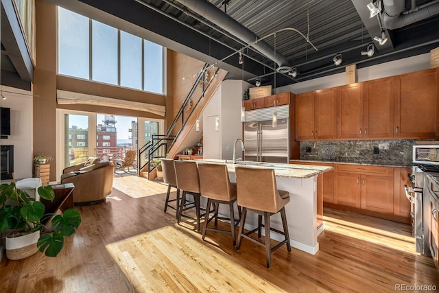 kitchen featuring a towering ceiling, light wood-style flooring, stainless steel built in fridge, a view of city, and a kitchen bar