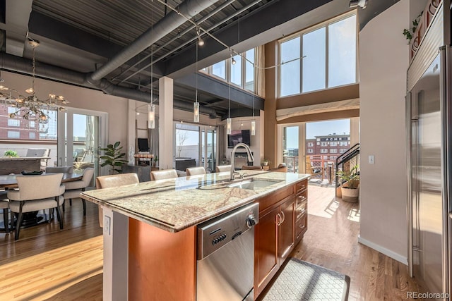 kitchen with stainless steel appliances, a high ceiling, a sink, open floor plan, and light wood finished floors