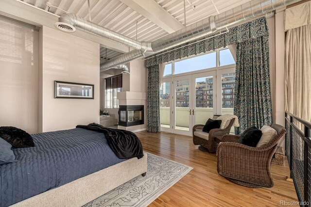 bedroom with a view of city, multiple windows, a multi sided fireplace, and wood finished floors