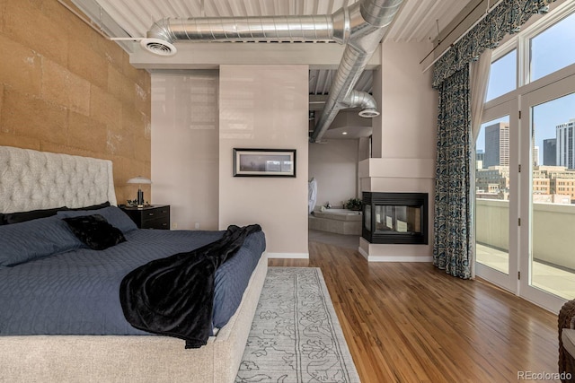 bedroom featuring a high ceiling, wood finished floors, visible vents, and a multi sided fireplace