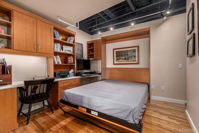 bedroom featuring light wood-type flooring, built in study area, rail lighting, and baseboards