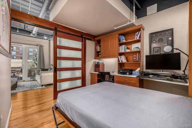 bedroom featuring light wood-style floors, access to outside, built in study area, and a barn door