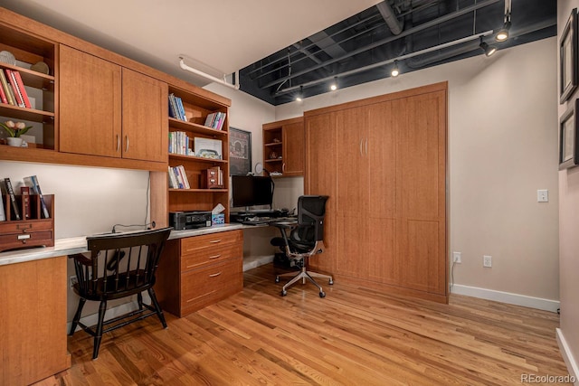 office space featuring baseboards, built in desk, track lighting, and light wood-style floors