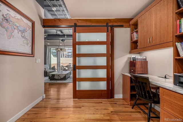 office space featuring light wood-type flooring, a barn door, baseboards, and built in desk