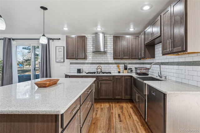 kitchen with light hardwood / wood-style floors, sink, decorative light fixtures, stainless steel appliances, and wall chimney exhaust hood