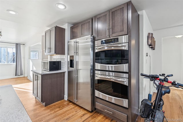 kitchen with dark brown cabinets, light wood-type flooring, tasteful backsplash, and stainless steel appliances