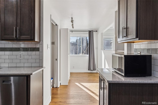 kitchen featuring fridge, tasteful backsplash, dark brown cabinetry, light hardwood / wood-style flooring, and dark stone counters