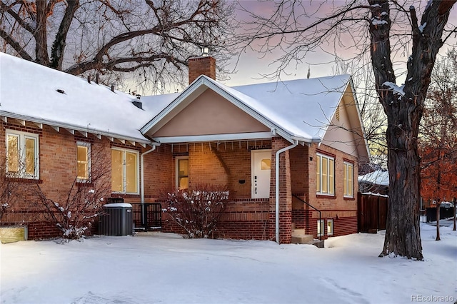 view of front facade featuring central AC, brick siding, a chimney, and a porch