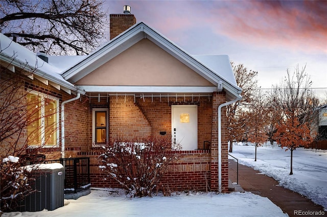 view of front of home featuring central air condition unit, brick siding, a chimney, and stucco siding