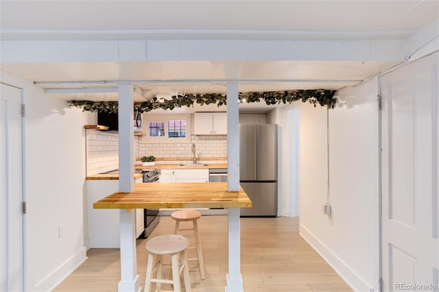 260 N Grant St, Denver, CO 80203 - kitchen featuring butcher block countertops, stainless steel appliances, a sink, decorative backsplash, and white cabinetry