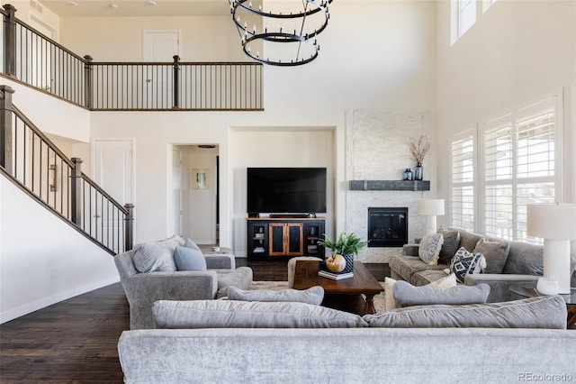 living area featuring a towering ceiling, a chandelier, dark wood finished floors, stairway, and baseboards