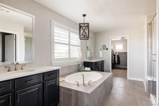 bathroom featuring a shower stall, a bath, two vanities, a walk in closet, and baseboards