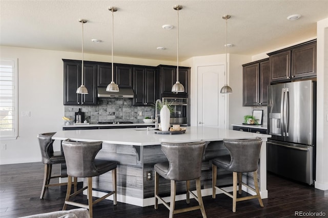 kitchen with appliances with stainless steel finishes, backsplash, light countertops, dark wood finished floors, and a kitchen breakfast bar