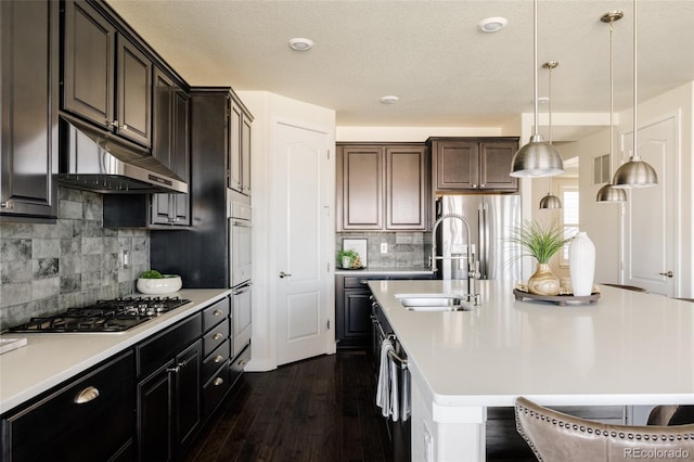 kitchen featuring under cabinet range hood, stainless steel appliances, light countertops, dark wood-type flooring, and decorative backsplash
