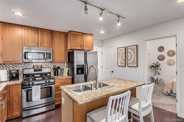 kitchen with sink, dark wood-type flooring, appliances with stainless steel finishes, a kitchen breakfast bar, and an island with sink