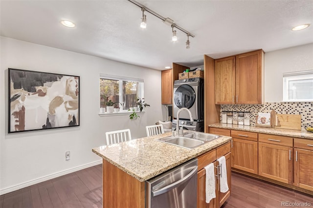 kitchen with dishwasher, sink, backsplash, stacked washer / drying machine, and a center island with sink