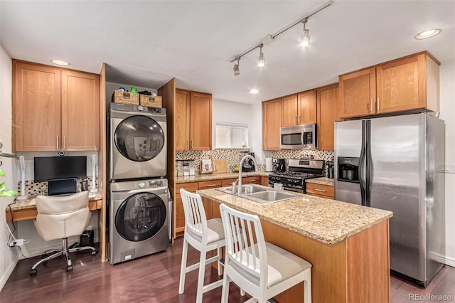 kitchen featuring stacked washing maching and dryer, sink, a kitchen breakfast bar, a kitchen island with sink, and stainless steel appliances