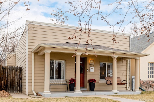 view of front of home with a porch, a shingled roof, and fence