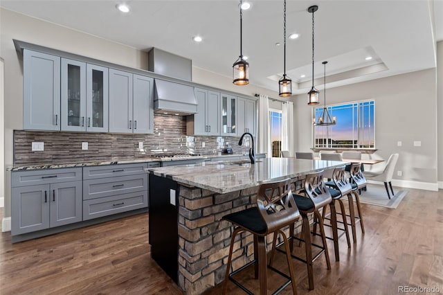 29303 E 165th Ave, Brighton, CO 80603 - kitchen with gray cabinetry, decorative backsplash, premium range hood, a center island with sink, and light stone counters