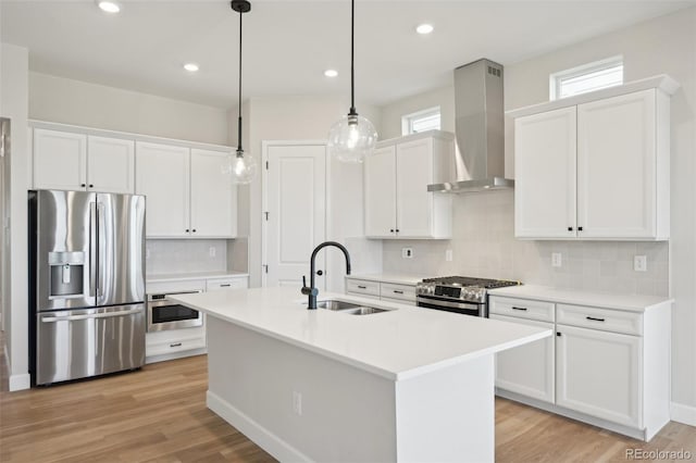 kitchen featuring appliances with stainless steel finishes, light wood-type flooring, wall chimney exhaust hood, sink, and hanging light fixtures