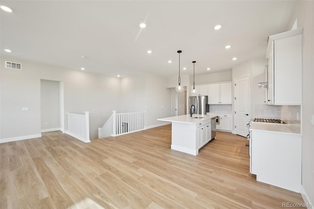 kitchen with pendant lighting, white cabinetry, an island with sink, and light hardwood / wood-style flooring