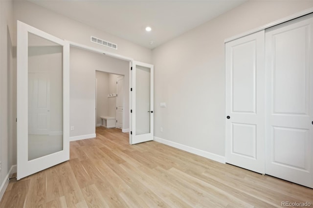 unfurnished bedroom featuring french doors, light hardwood / wood-style floors, and a closet