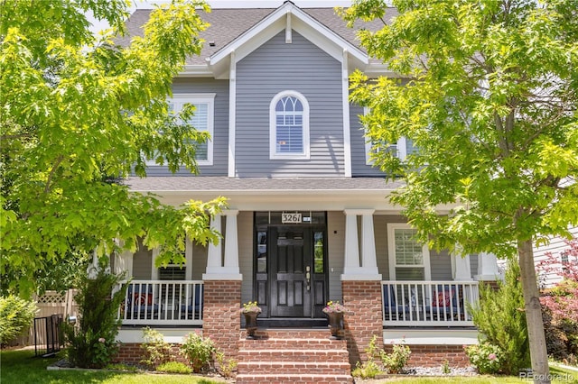 view of front of property featuring a porch, brick siding, and roof with shingles