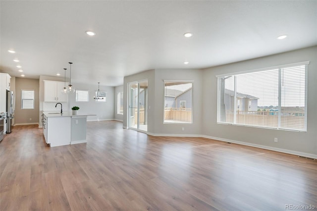 kitchen with sink, light hardwood / wood-style flooring, white cabinets, hanging light fixtures, and an island with sink