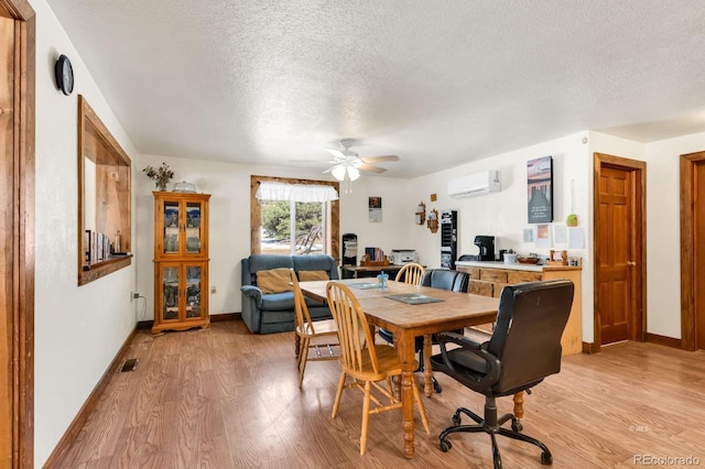 dining space with an AC wall unit, ceiling fan, light hardwood / wood-style floors, and a textured ceiling