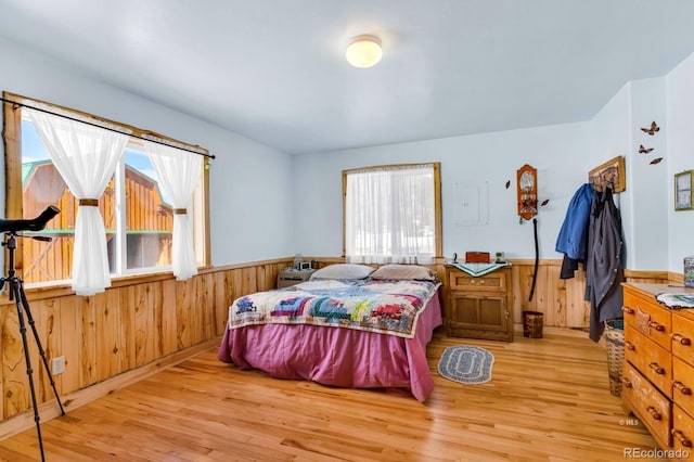 bedroom with light hardwood / wood-style flooring, multiple windows, and wood walls