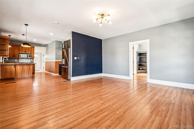 unfurnished living room featuring visible vents, light wood-style flooring, baseboards, and a sink