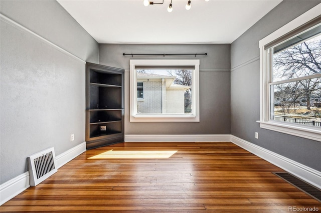 empty room with visible vents, plenty of natural light, baseboards, and wood-type flooring