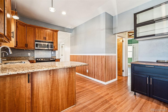 kitchen featuring light wood finished floors, stainless steel microwave, range with gas cooktop, a wainscoted wall, and a sink