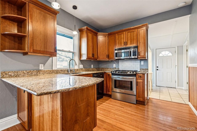 kitchen with brown cabinets, a sink, light stone counters, appliances with stainless steel finishes, and a peninsula