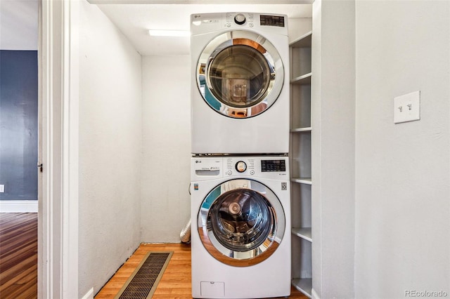 laundry room with visible vents, stacked washer and dryer, wood finished floors, and laundry area