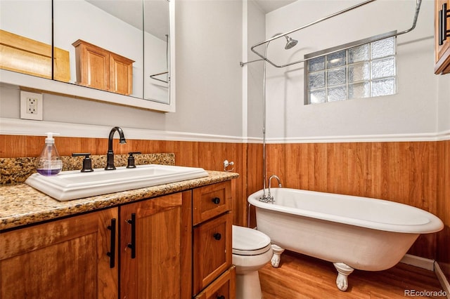 bathroom with wooden walls, wainscoting, a freestanding tub, wood finished floors, and vanity