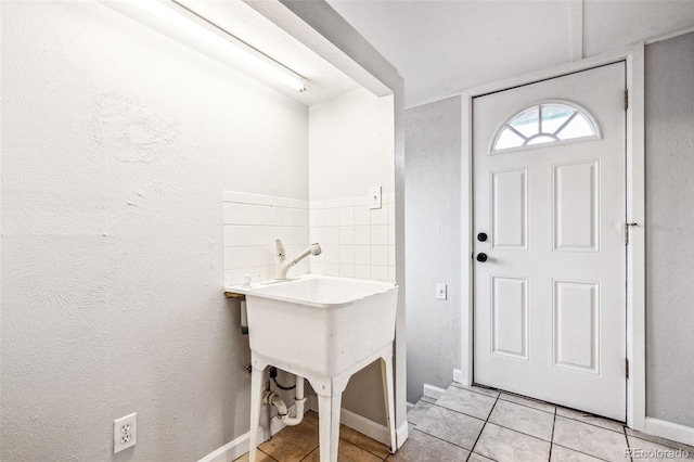 clothes washing area with light tile patterned floors, baseboards, and a textured wall