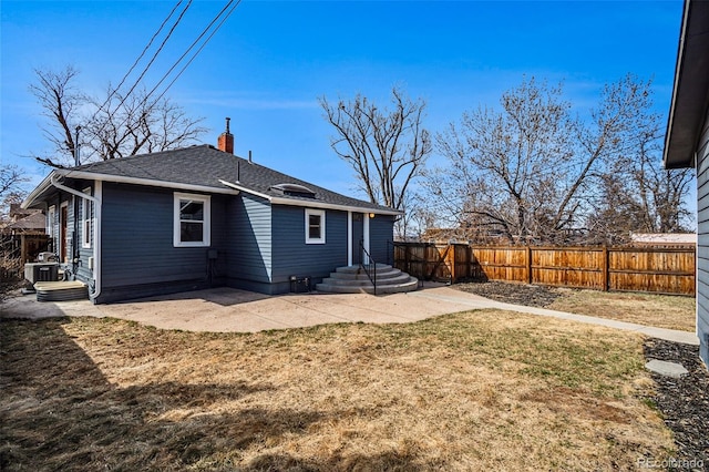 rear view of house featuring a shingled roof, fence, a chimney, a yard, and a patio