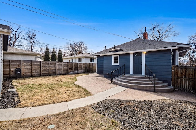 rear view of property featuring a fenced backyard, roof with shingles, and a chimney