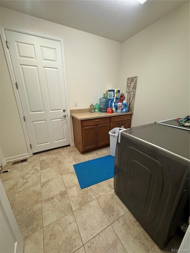 clothes washing area with cabinets, washer / dryer, and light tile patterned floors