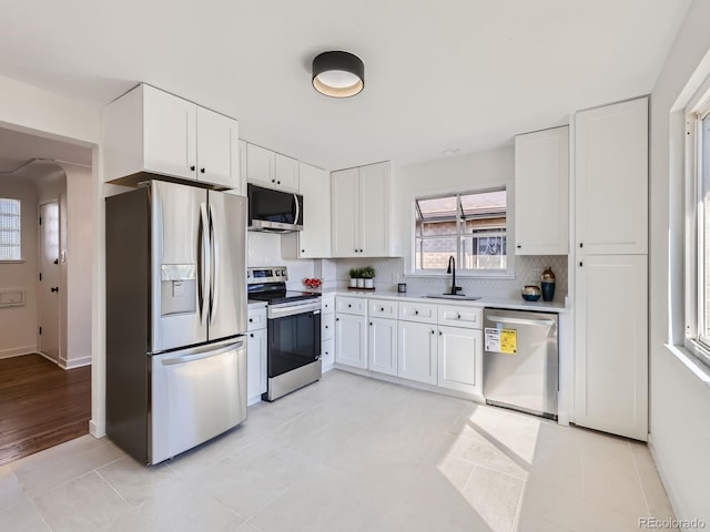 kitchen featuring appliances with stainless steel finishes, sink, decorative backsplash, white cabinetry, and light tile patterned flooring