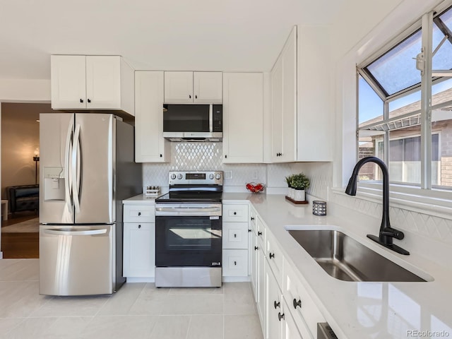 kitchen with white cabinetry, backsplash, light tile patterned floors, stainless steel appliances, and sink