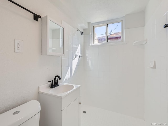 bathroom with vanity, toilet, a tile shower, and a textured ceiling