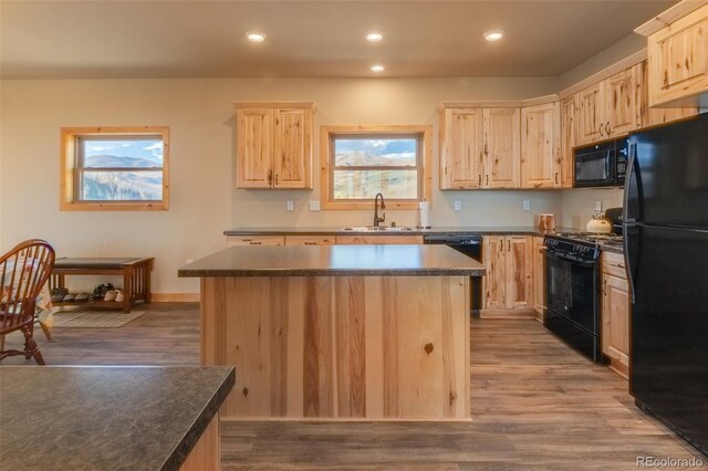 kitchen featuring light brown cabinets, a center island, dark countertops, black appliances, and a sink