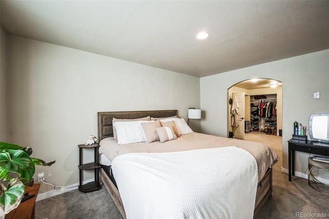 bedroom featuring arched walkways, baseboards, a closet, dark colored carpet, and a walk in closet