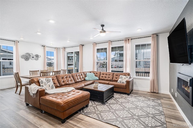 living room featuring ceiling fan, a large fireplace, a textured ceiling, and light hardwood / wood-style flooring