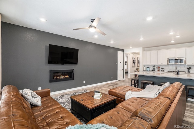 living room featuring ceiling fan, sink, and light wood-type flooring