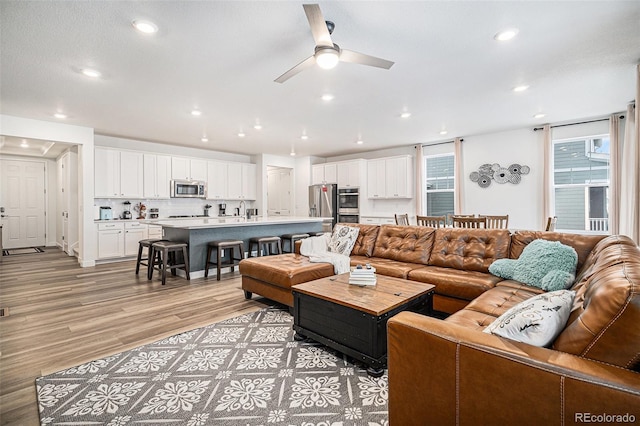 living room featuring ceiling fan, sink, and light wood-type flooring