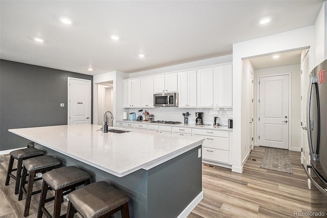 kitchen featuring appliances with stainless steel finishes, white cabinetry, sink, light stone countertops, and a center island with sink