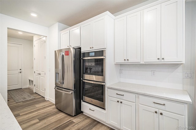 kitchen featuring dark hardwood / wood-style floors, white cabinetry, decorative backsplash, stainless steel appliances, and light stone countertops